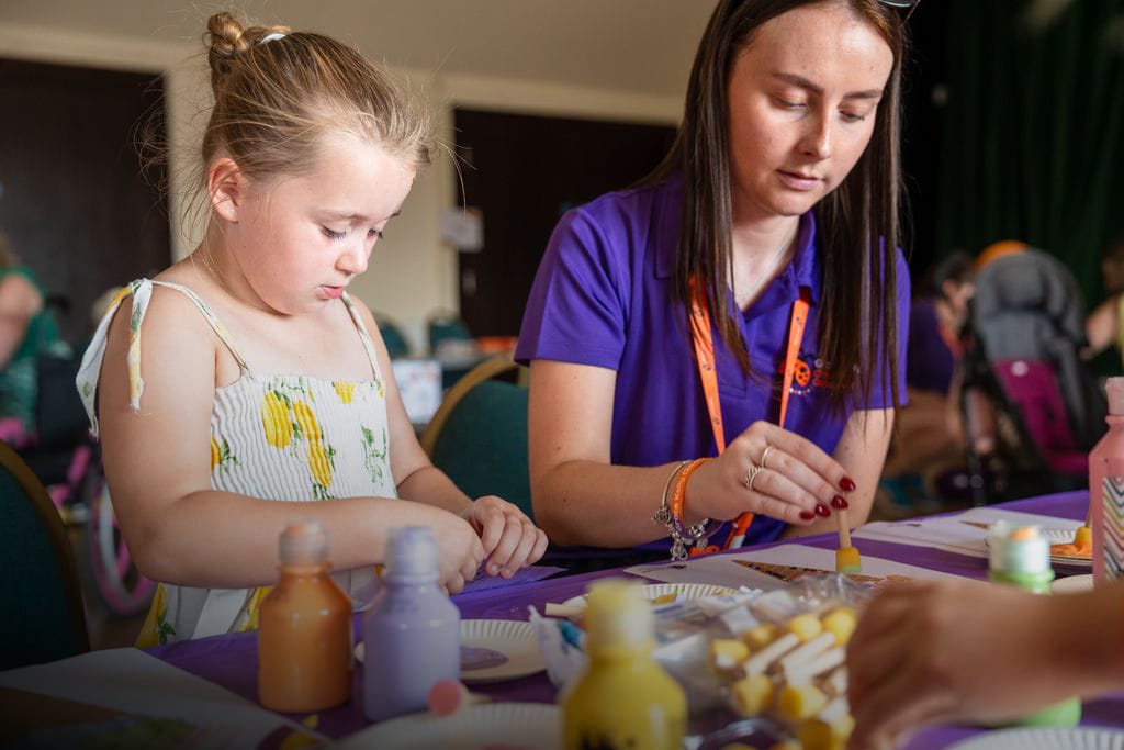 A young girl and charity volunteer paint together at a craft table
